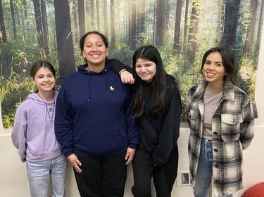 Group of 4 females standing together, smiling for photo