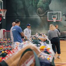 Five staff standing at tables filled with food hamper bags, waiting for participants to arrive to hand them out